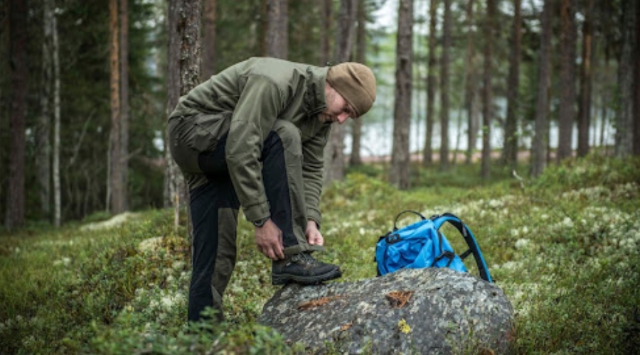 Muž v outdoorovom oblečení v lese s batohom.