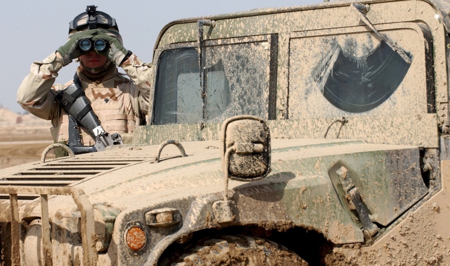 Vojak stojaci pri zablatenom Hummer pozerajúc ďalekohľadom
